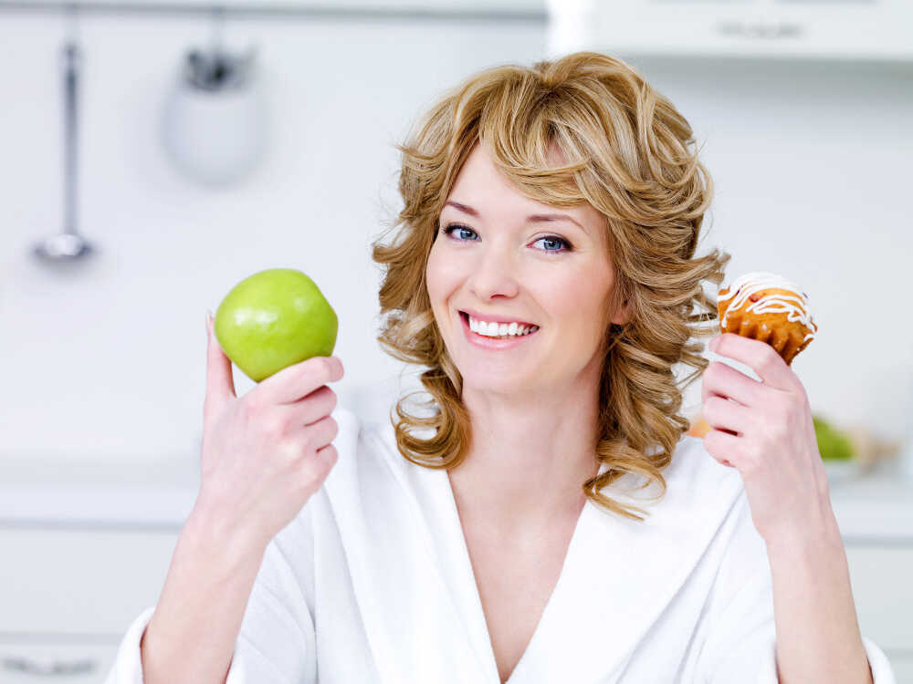 dieta po wybielaniu zębów kobieta pokazuje jabłko i słodycze